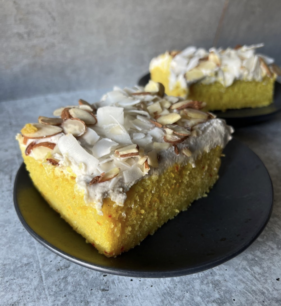 Saffron cake slice with cardamom coconut cream frosting, almonds, and coconut flakes