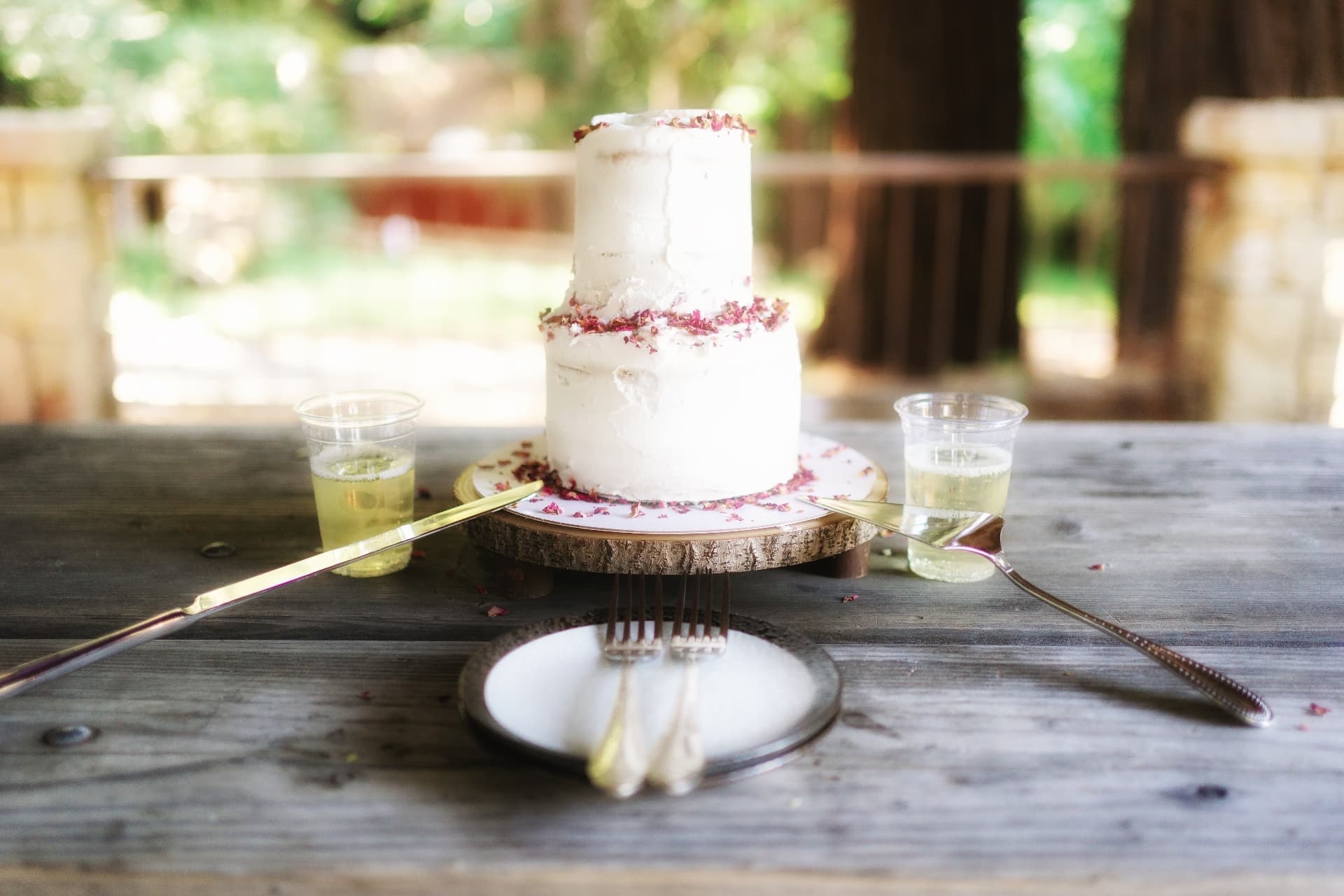 Two-tier vegan wedding cake with dried rose petals on a wooden slab